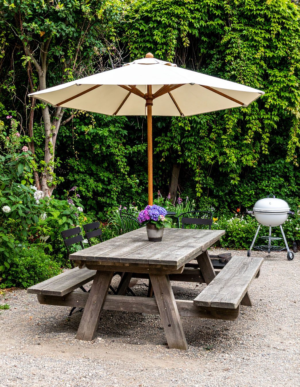 Table de pique-nique en bois rustique avec bancs sous un parasol, entourée de verdure