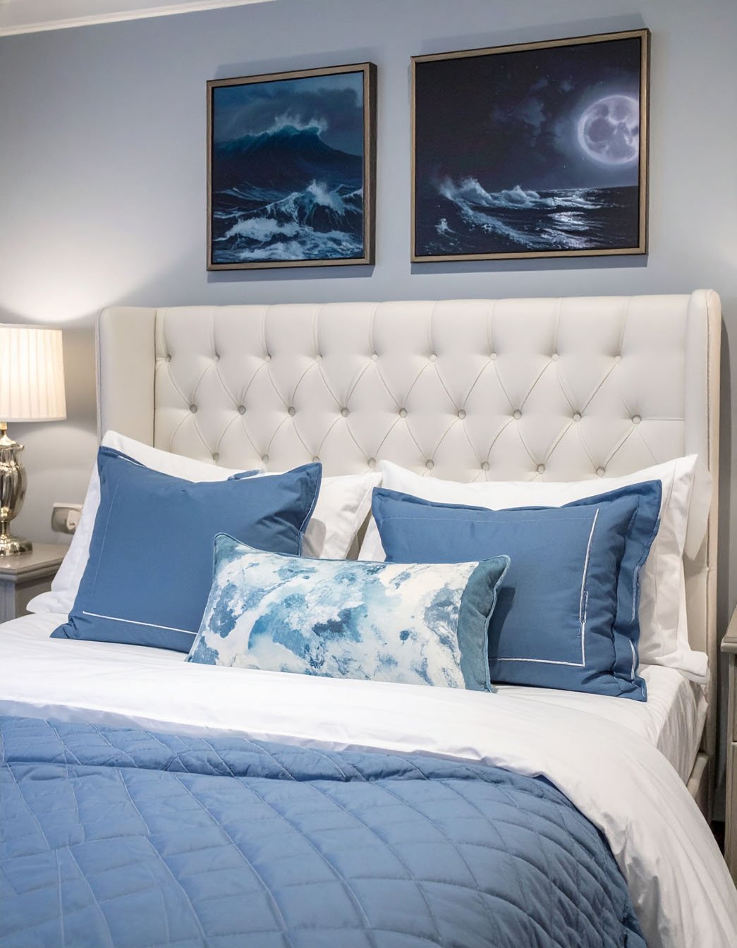 Chambre avec tête de lit capitonnée blanche, literie bleue, tableaux de vagues nocturnes