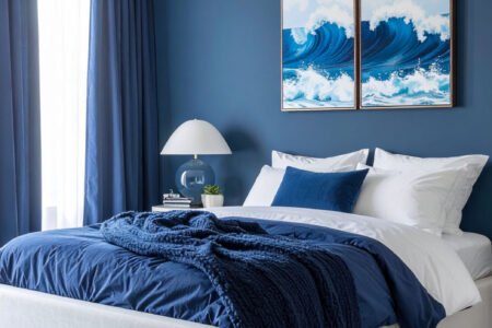 Chambre aux murs et rideaux bleu profond, lit blanc, plaid et tableaux de vagues