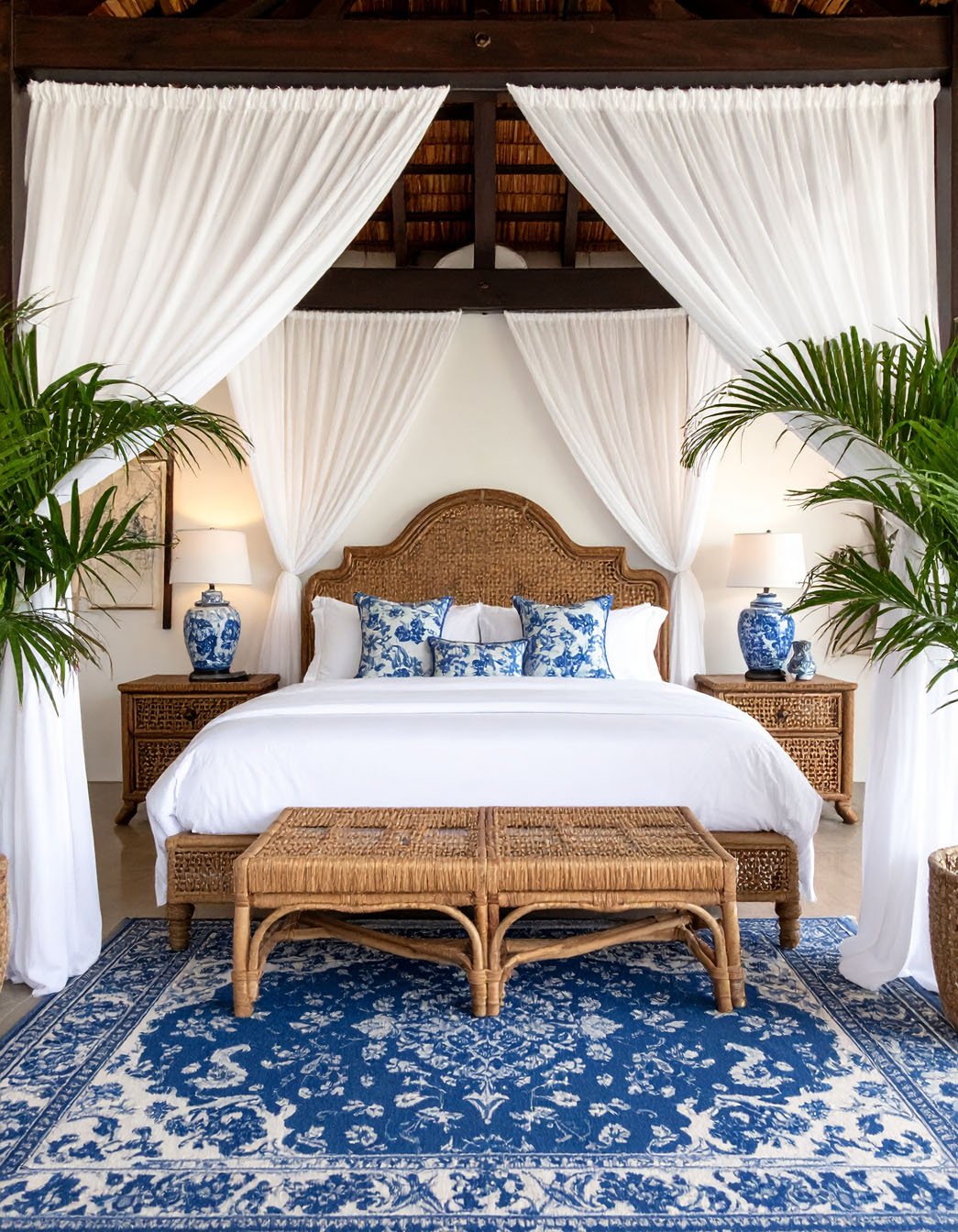 Chambre luxueuse avec lit en rotin, voilages blancs, tapis bleu et blanc, plantes