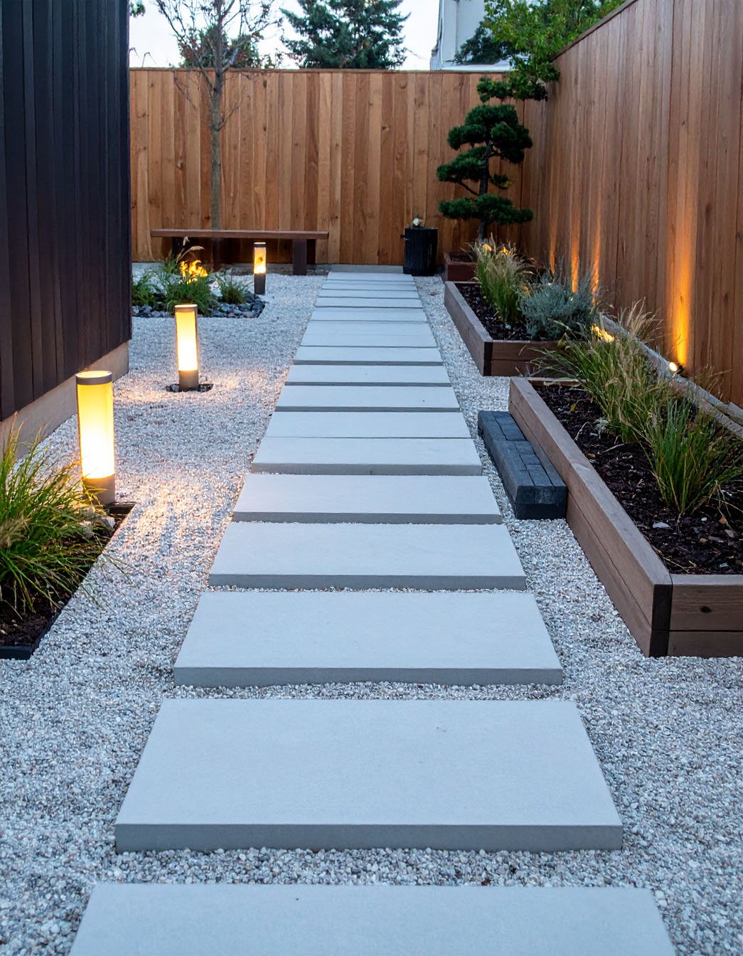Chemin de dalles sur gravier, jardinières en bois et éclairage doux