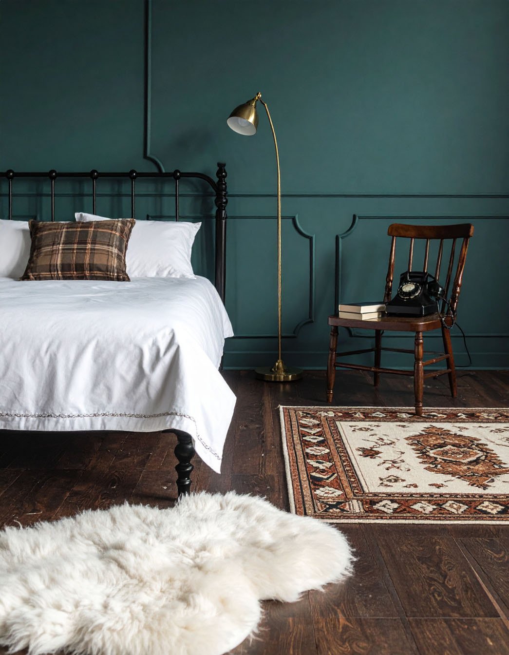 Chambre avec murs vert foncé à moulures, lit en fer forgé noir et tapis en peau de mouton