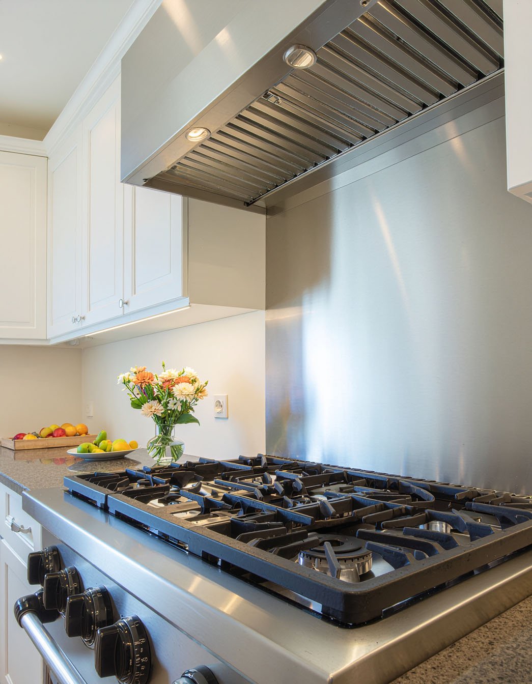 Gros plan sur une plaque de cuisson gaz avec crédence et hotte en inox