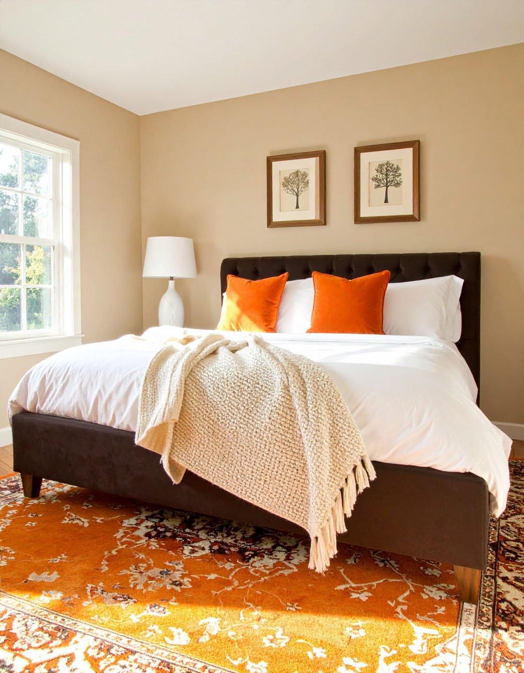 Chambre avec murs beiges, lit avec coussins orange vif et tapis orange à motifs