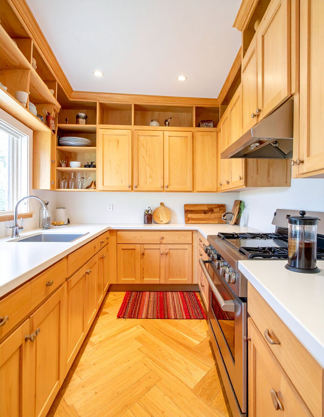 Cuisine en U avec meubles en bois clair, parquet à chevrons et petit tapis coloré