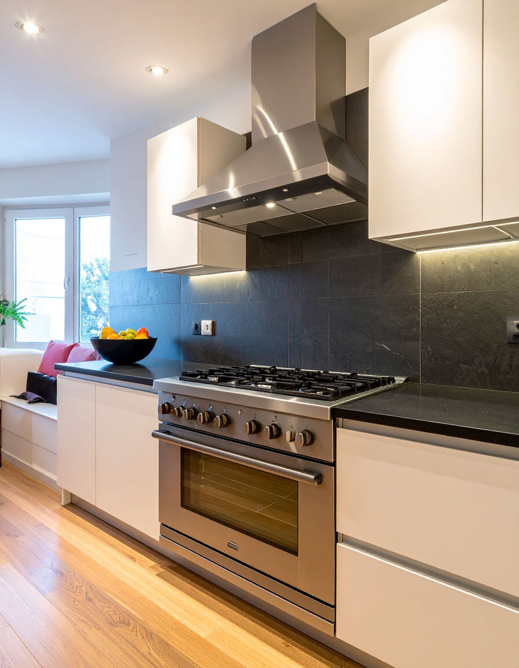 Cuisine avec meubles blancs, crédence en larges carreaux foncés et piano de cuisson inox