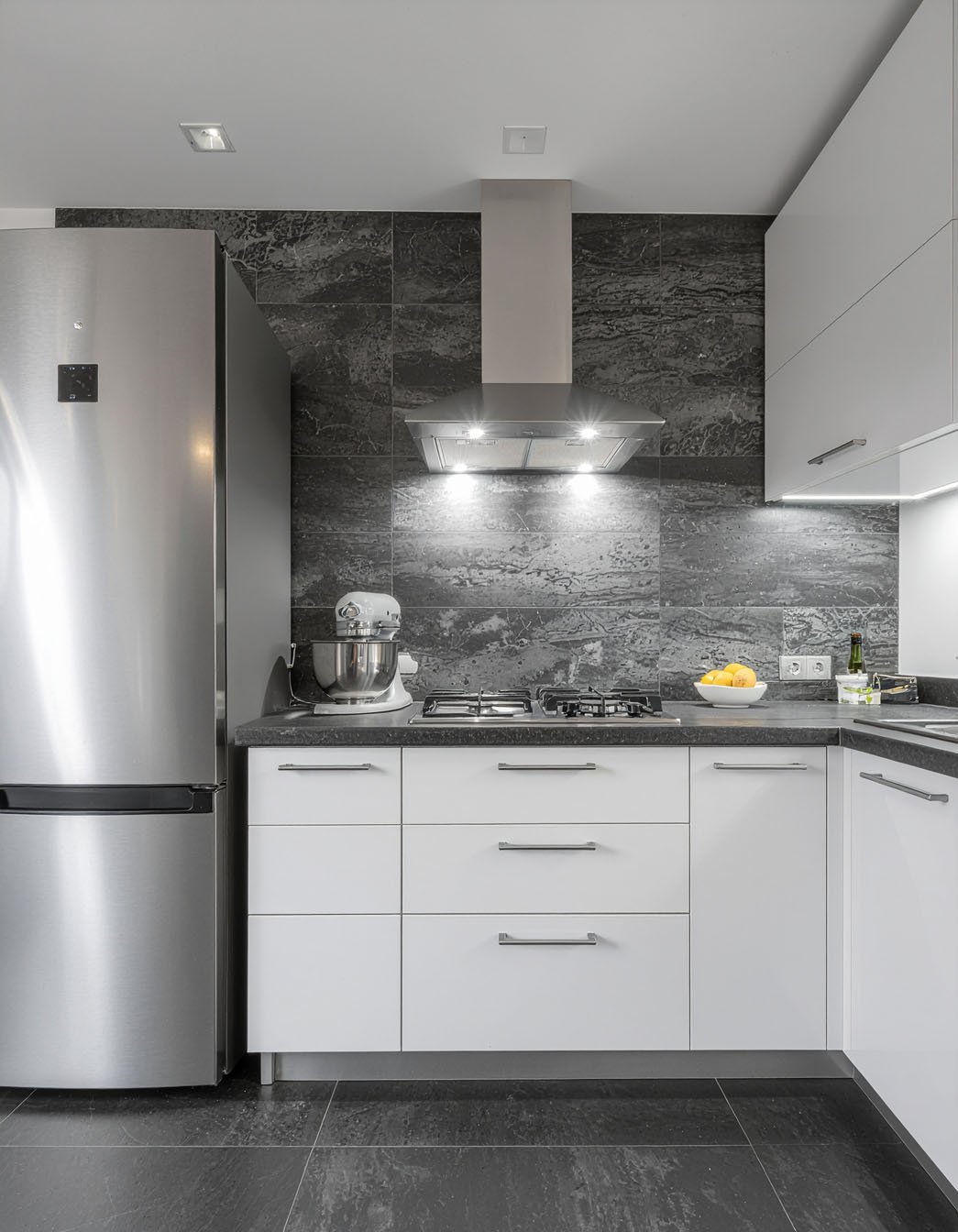 Cuisine moderne avec meubles blancs, crédence et sol en grands carreaux imitation pierre foncée