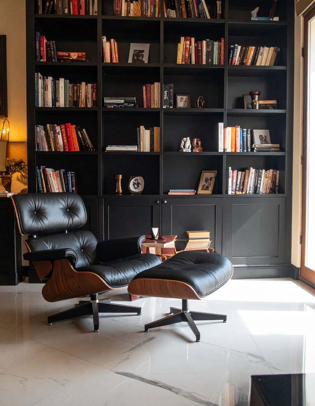 Coin lecture avec fauteuil en cuir noir et ottoman devant une grande bibliothèque noire