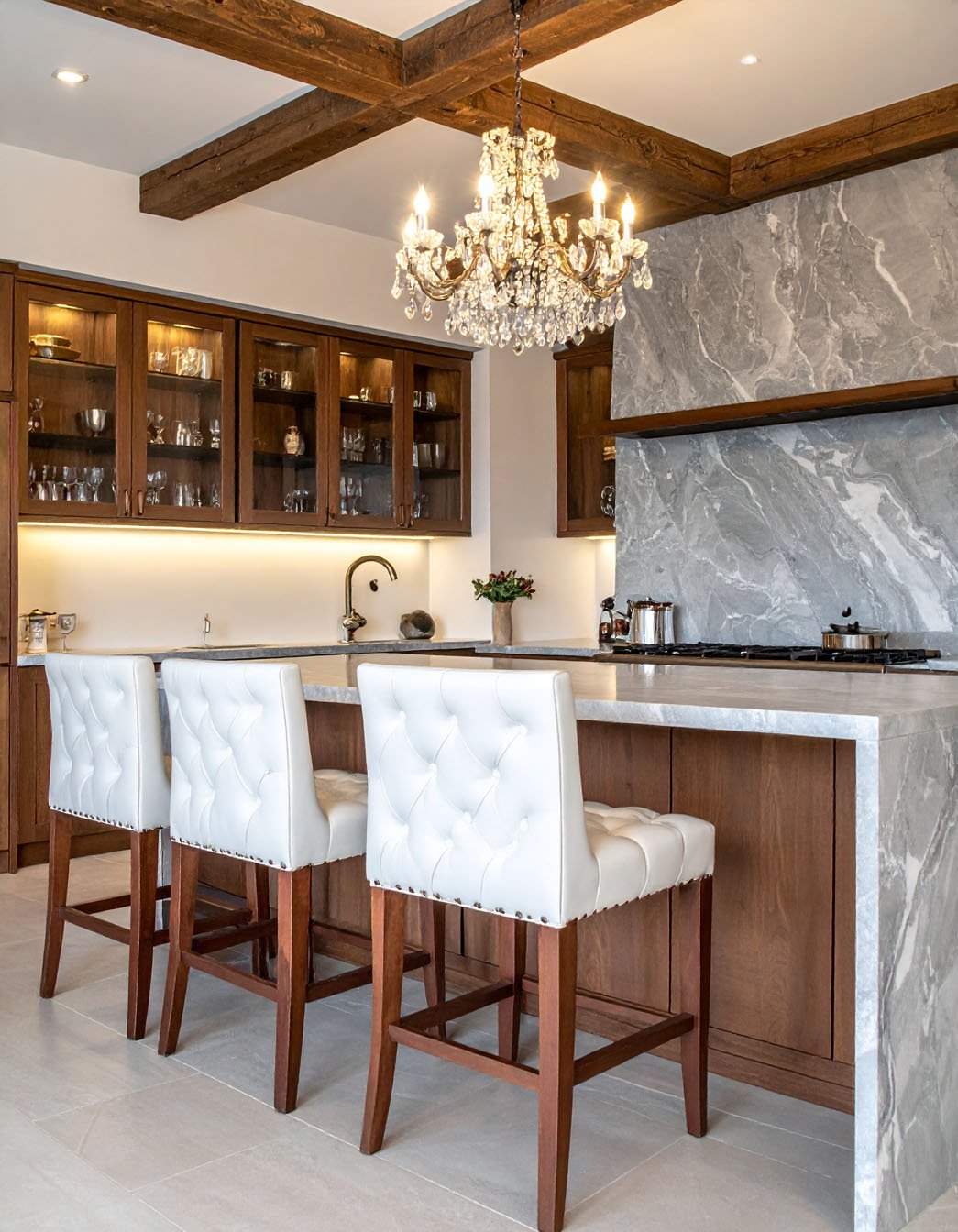 Cuisine avec îlot et crédence en marbre gris, tabourets hauts blancs et lustre en cristal