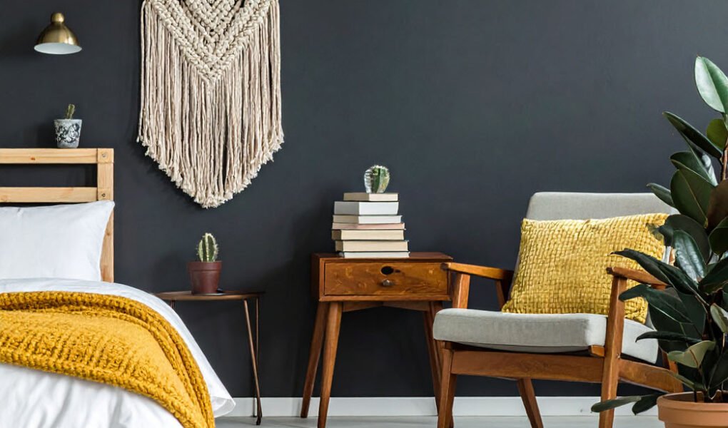 Chambre avec mur noir, lit avec plaid moutarde, fauteuil en bois et macramé mural