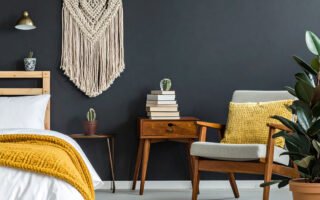 Chambre avec mur noir, lit avec plaid moutarde, fauteuil en bois et macramé mural