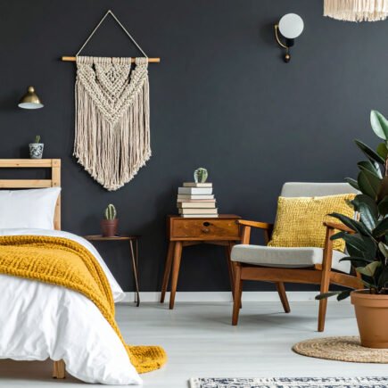 Chambre avec mur noir, lit avec plaid moutarde, fauteuil en bois et macramé mural