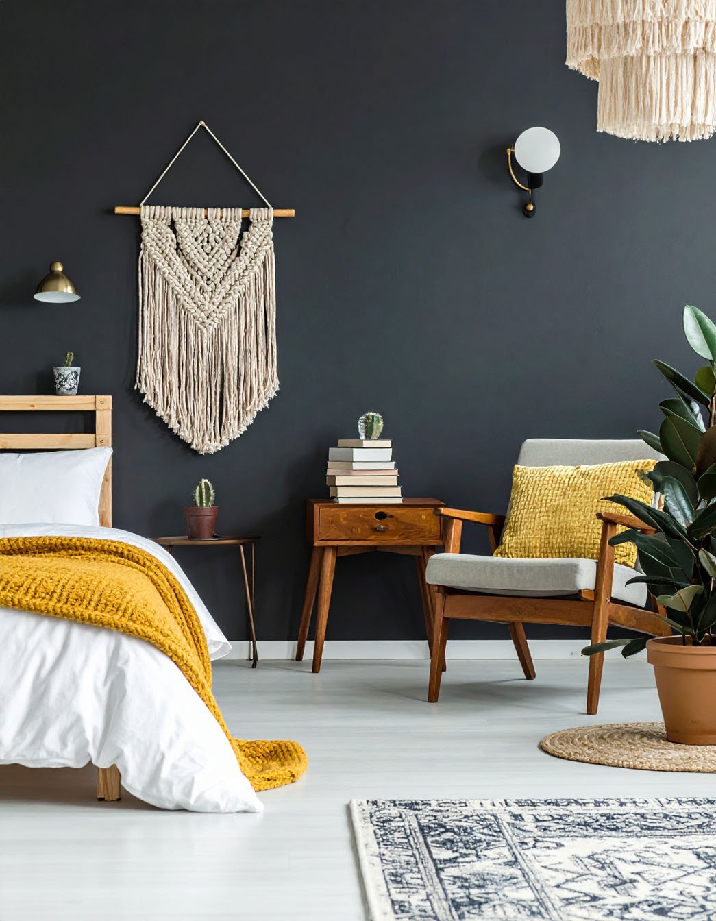 Chambre avec mur noir, lit avec plaid moutarde, fauteuil en bois et macramé mural
