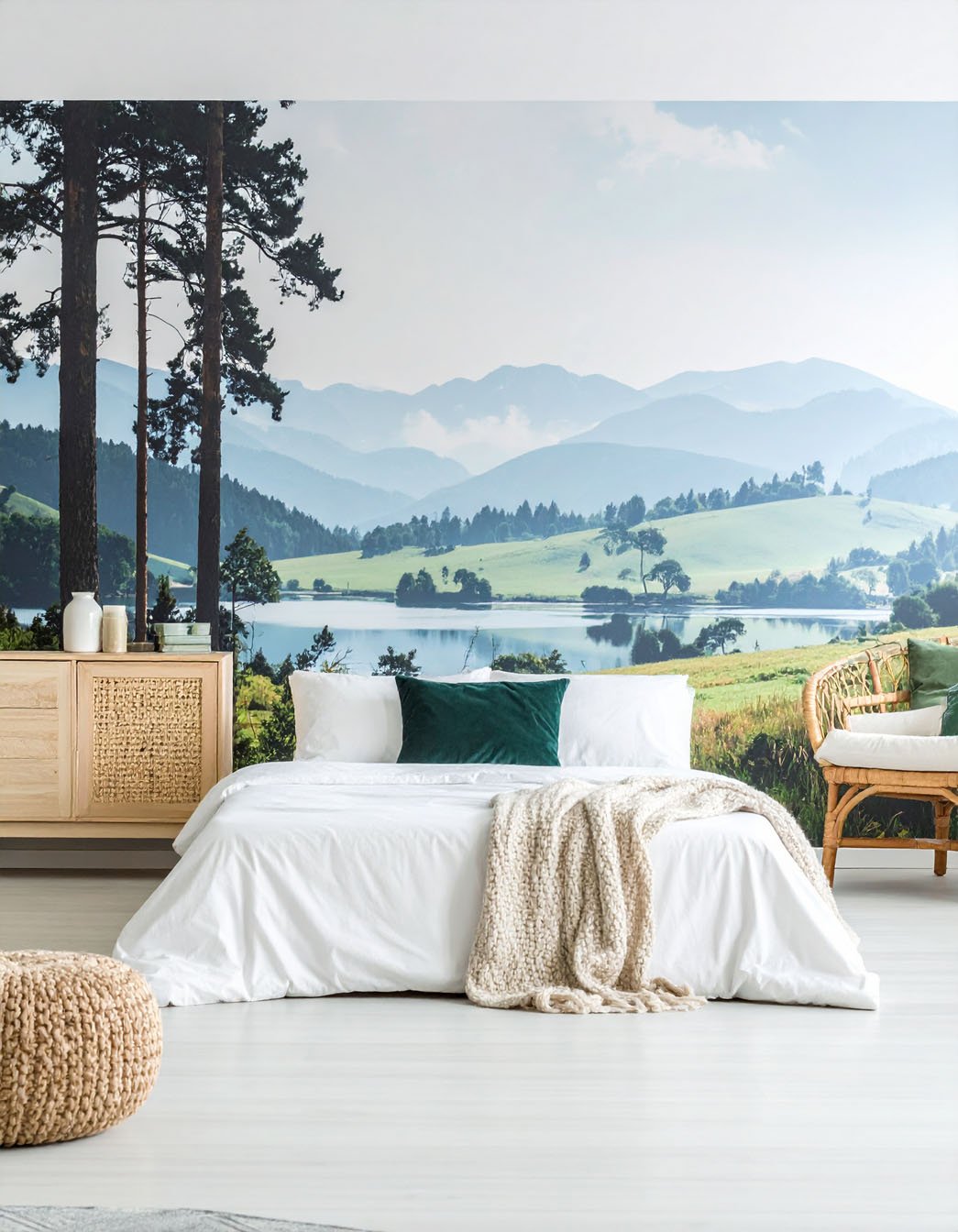 Chambre avec lit blanc, fauteuil en rotin et papier peint panoramique de paysage lacustre et montagneux