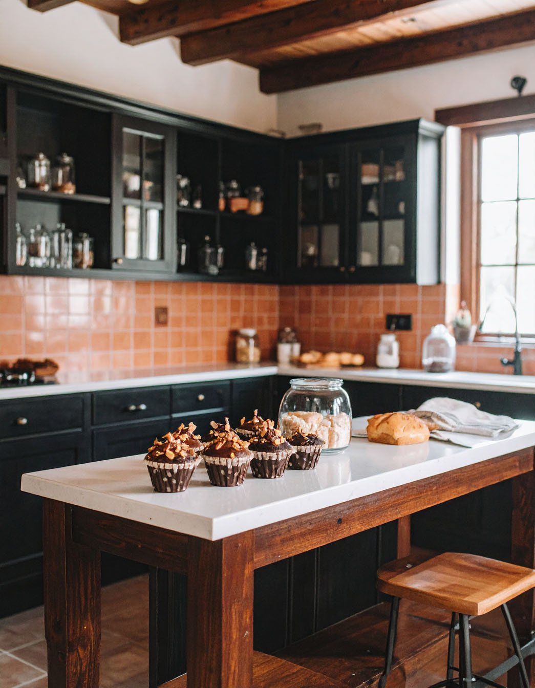 Cuisine rustique avec meubles noirs, îlot avec plan de travail blanc et muffins au chocolat
