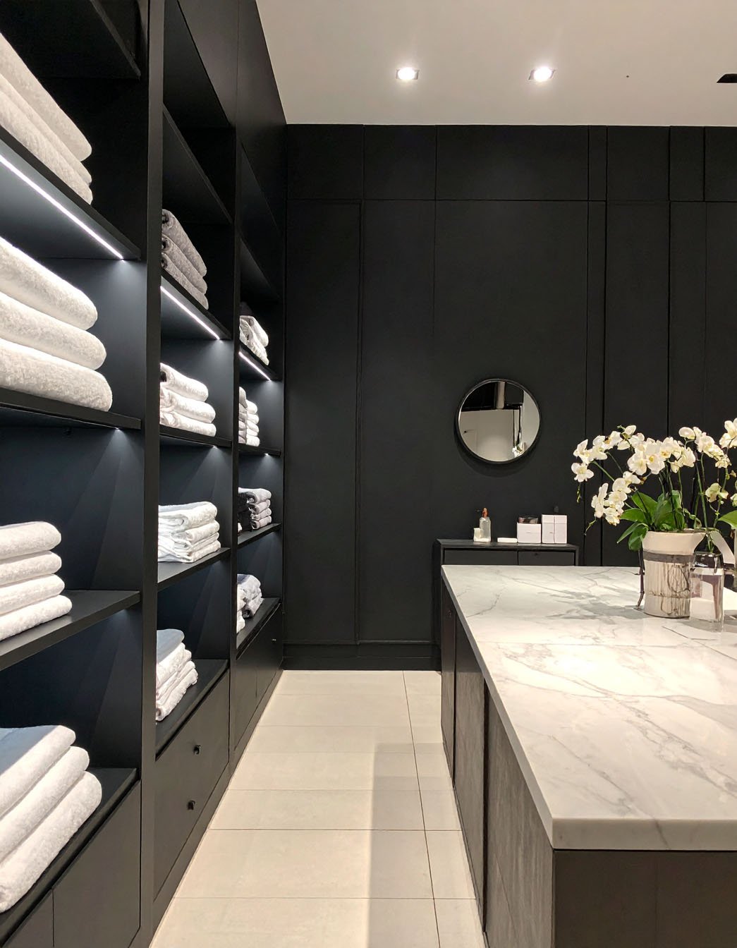 Dressing ou buanderie avec étagères noires éclairées, serviettes pliées et comptoir effet marbre