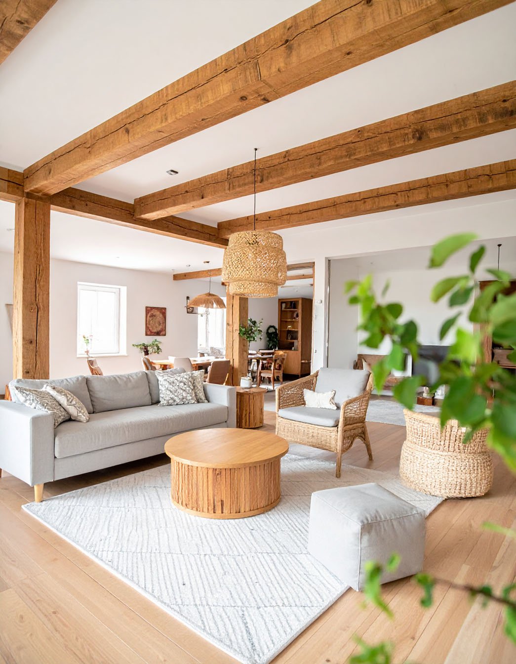 Salon avec poutres apparentes en bois, canapé gris, fauteuil en rotin et table basse ronde en bois