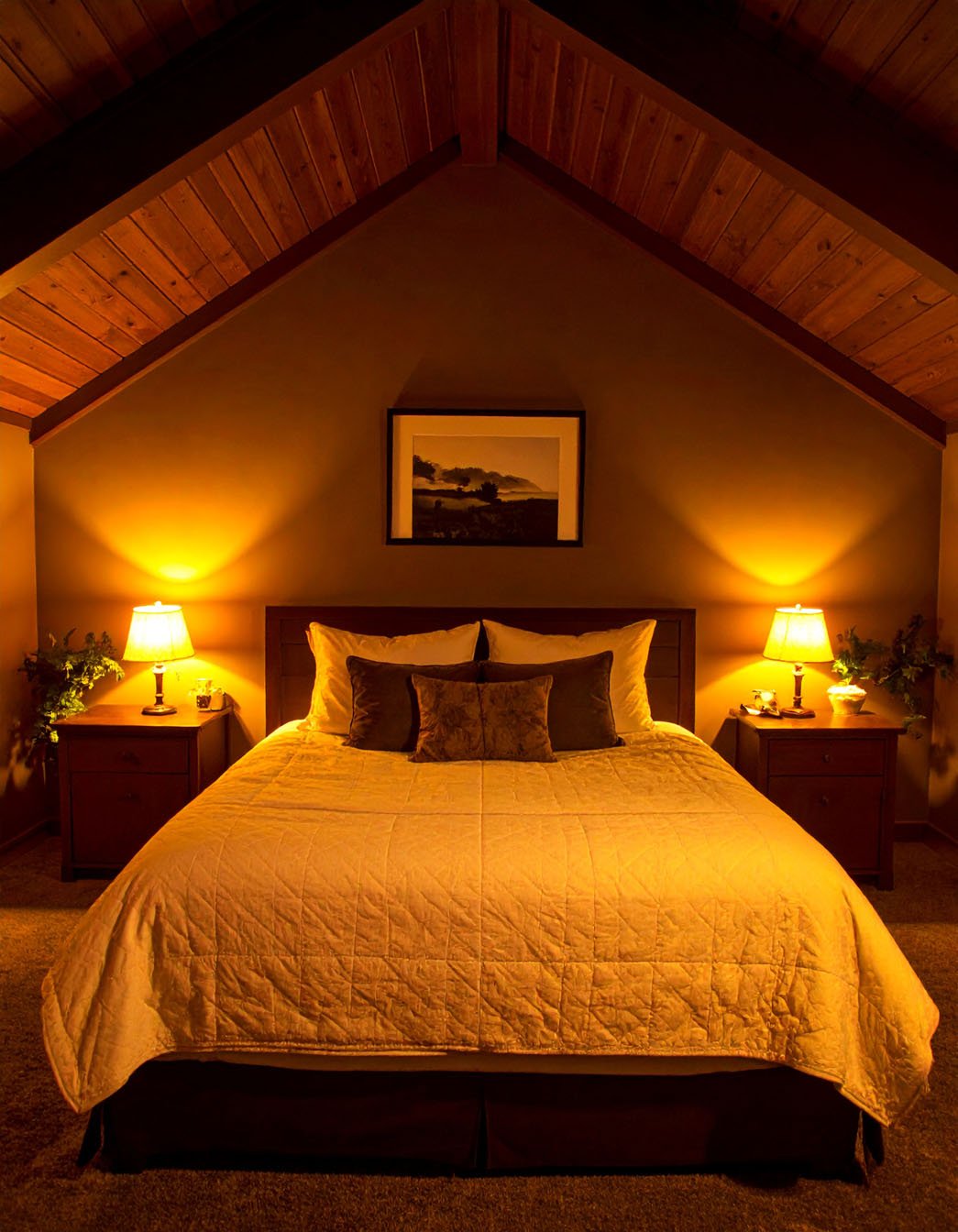 Chambre mansardée avec éclairage tamisé, lit avec couvre-lit matelassé et chevets en bois
