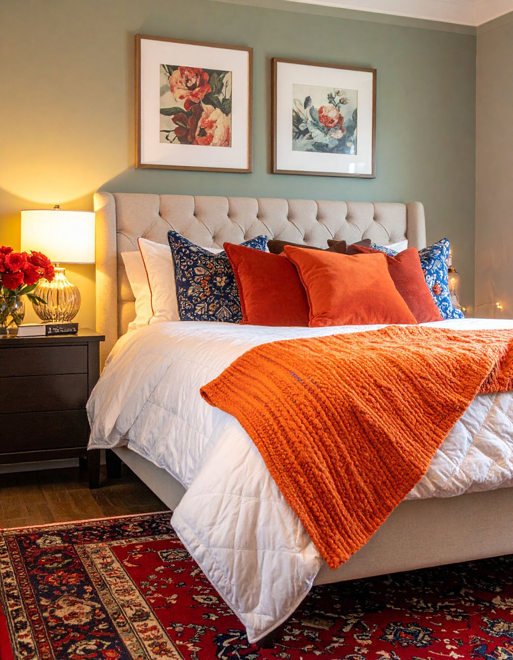 Chambre avec murs vert olive, lit avec coussins et plaid orange vif, tapis persan