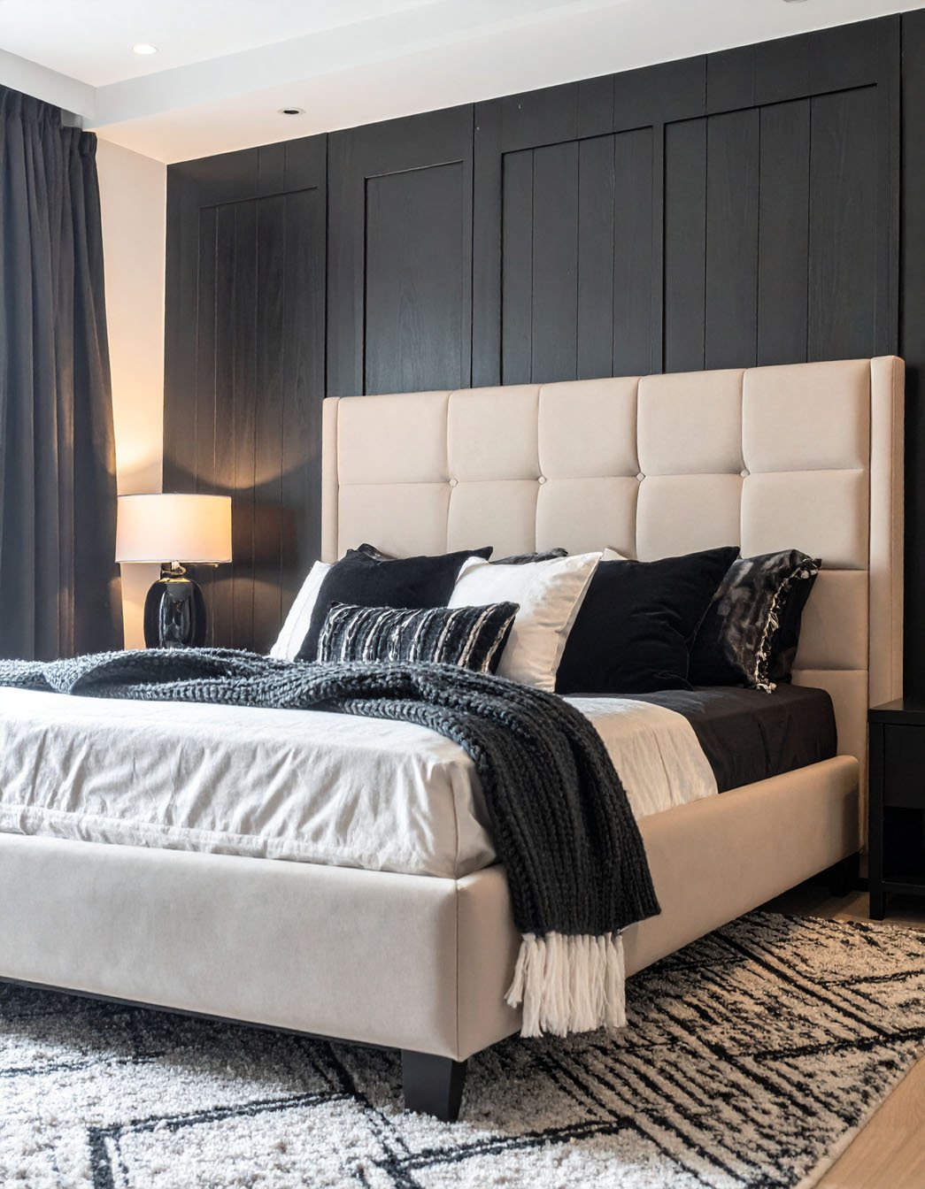 Chambre avec mur d'accent en lambris noir, lit beige et tapis à motifs graphiques