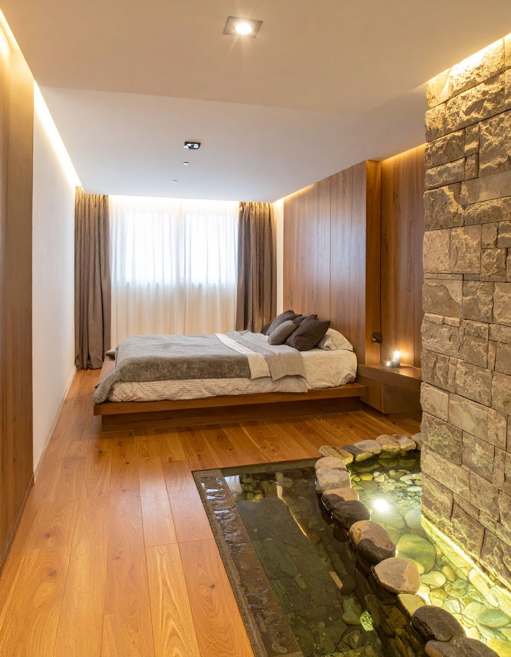 Chambre avec lit sur estrade en bois, mur en pierres et petit bassin intérieur