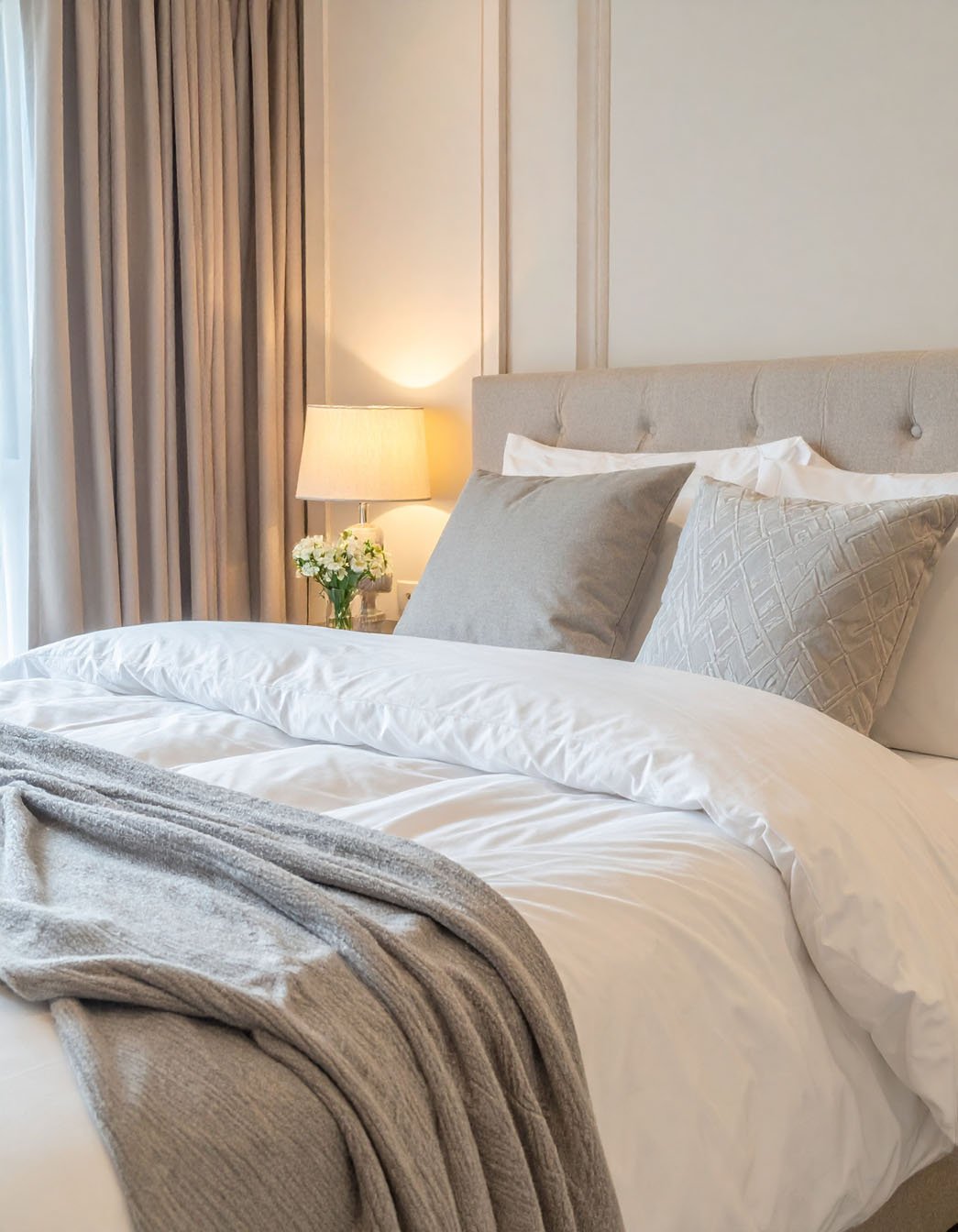 Chambre avec tête de lit capitonnée beige, literie blanche et plaid gris
