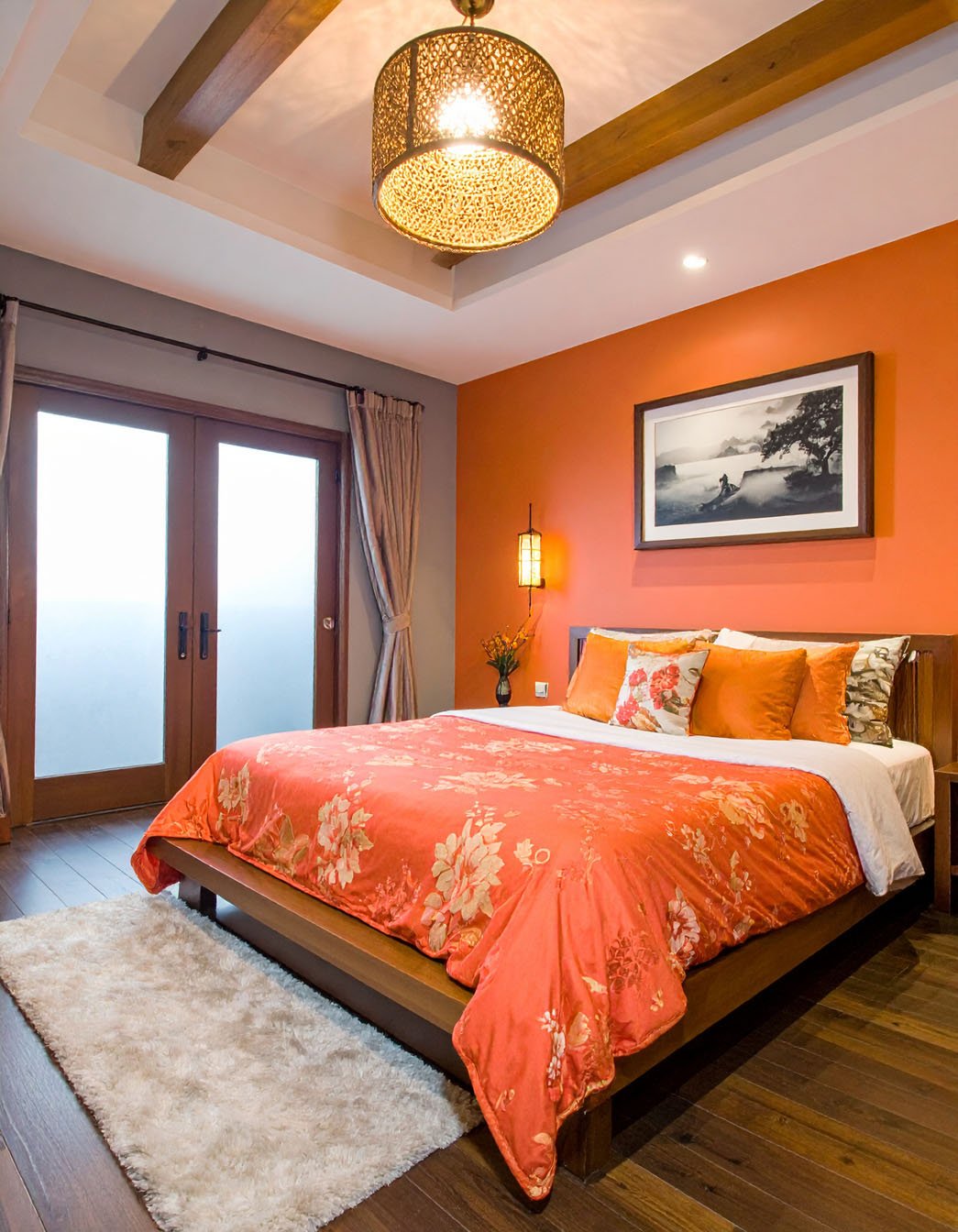 Chambre avec murs orange vif, lit en bois, parure florale orange et suspension en rotin