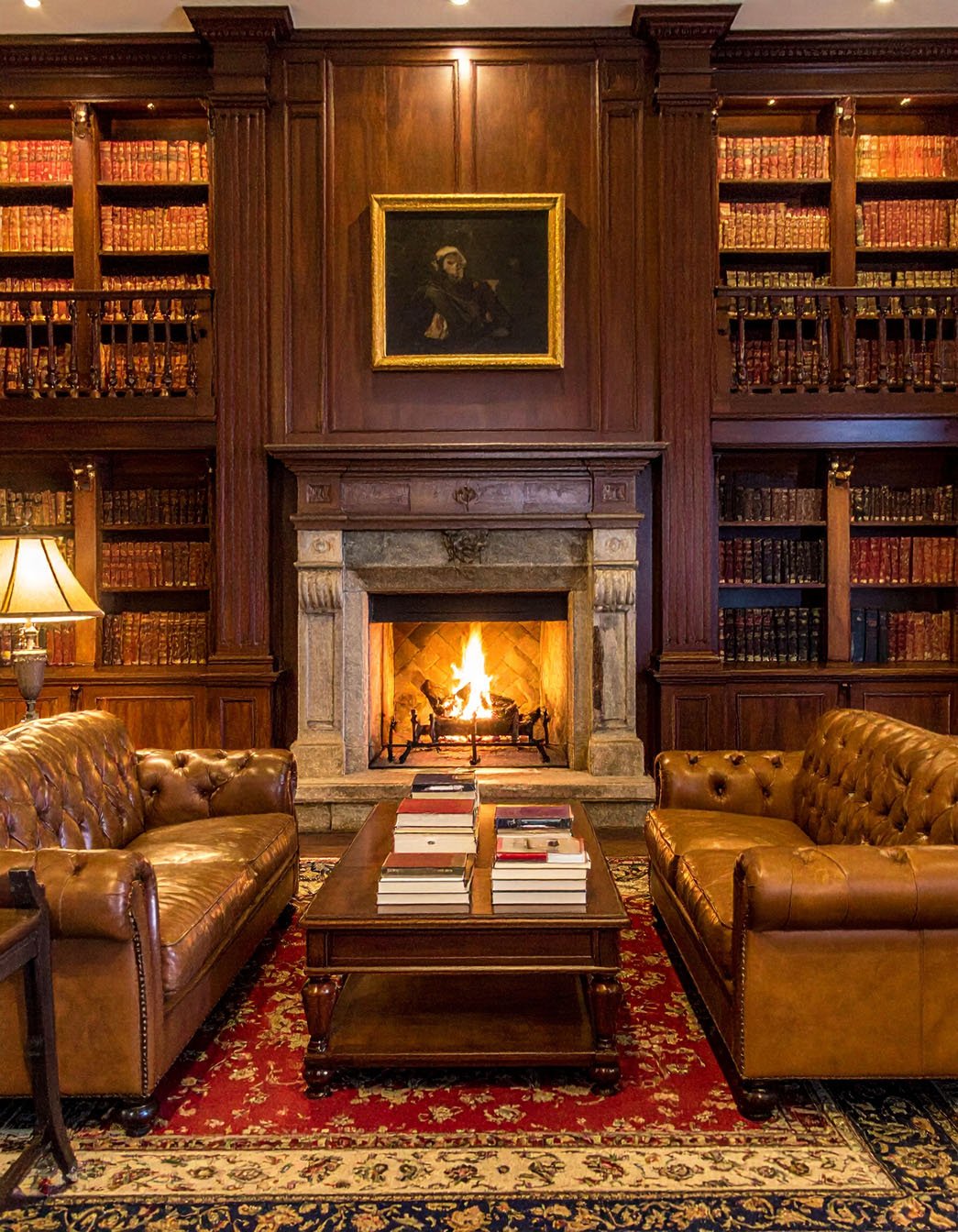 Bibliothèque lambrissée avec canapés Chesterfield en cuir marron et cheminée allumée