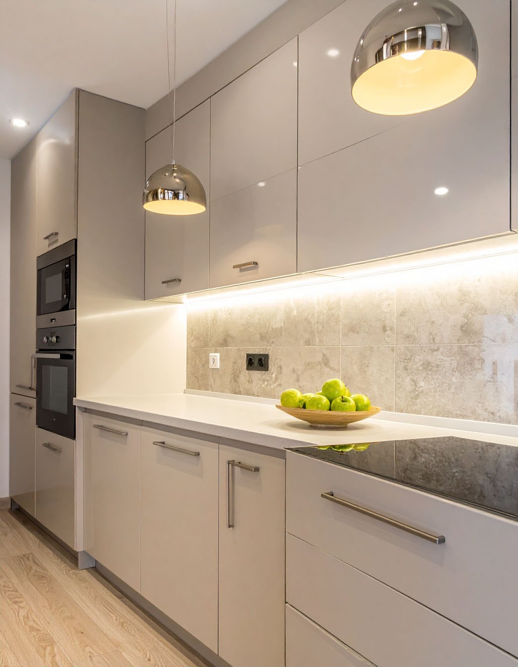 Cuisine avec meubles beige laqué, crédence en carreaux clairs et suspensions chromées