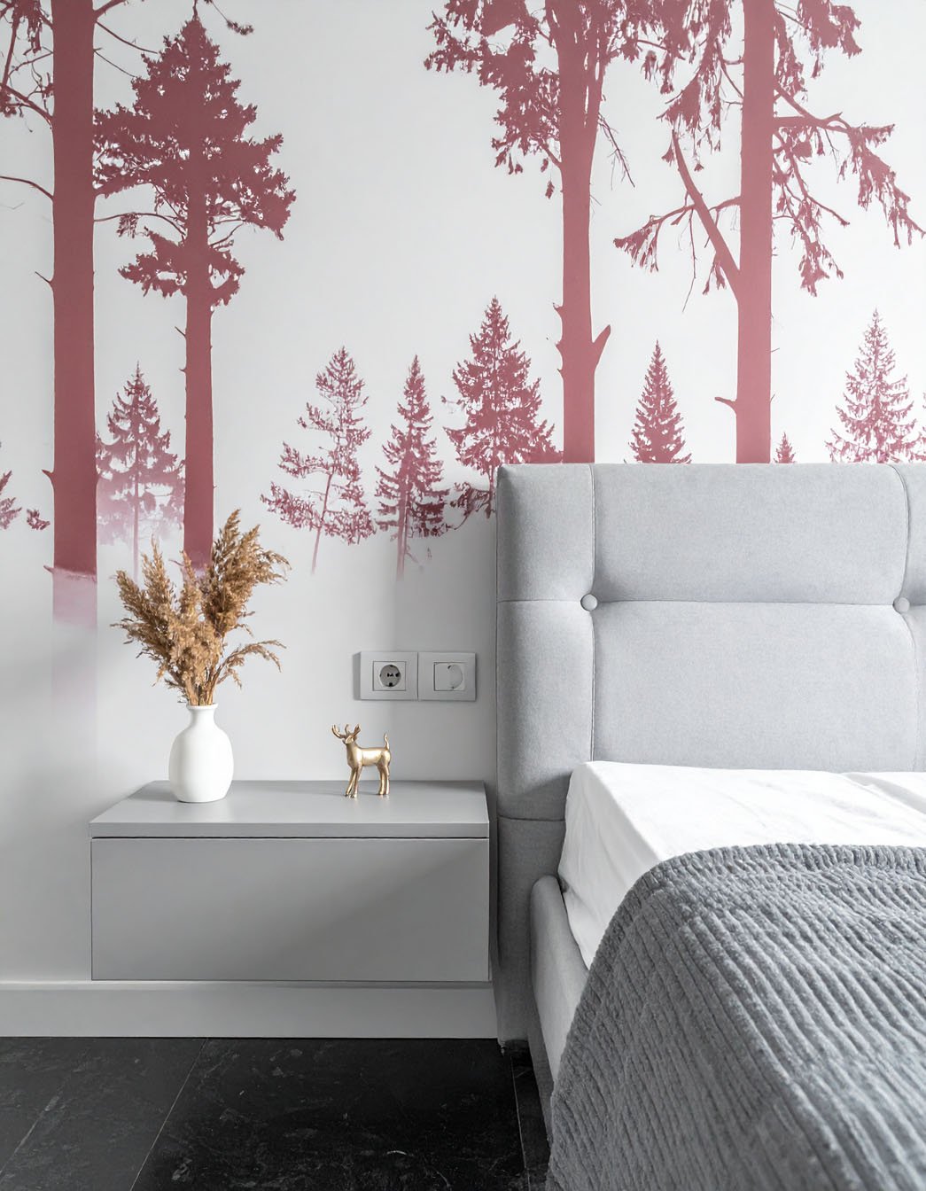 Chambre avec lit gris, table de chevet grise et papier peint à motif de silhouettes d'arbres rose foncé