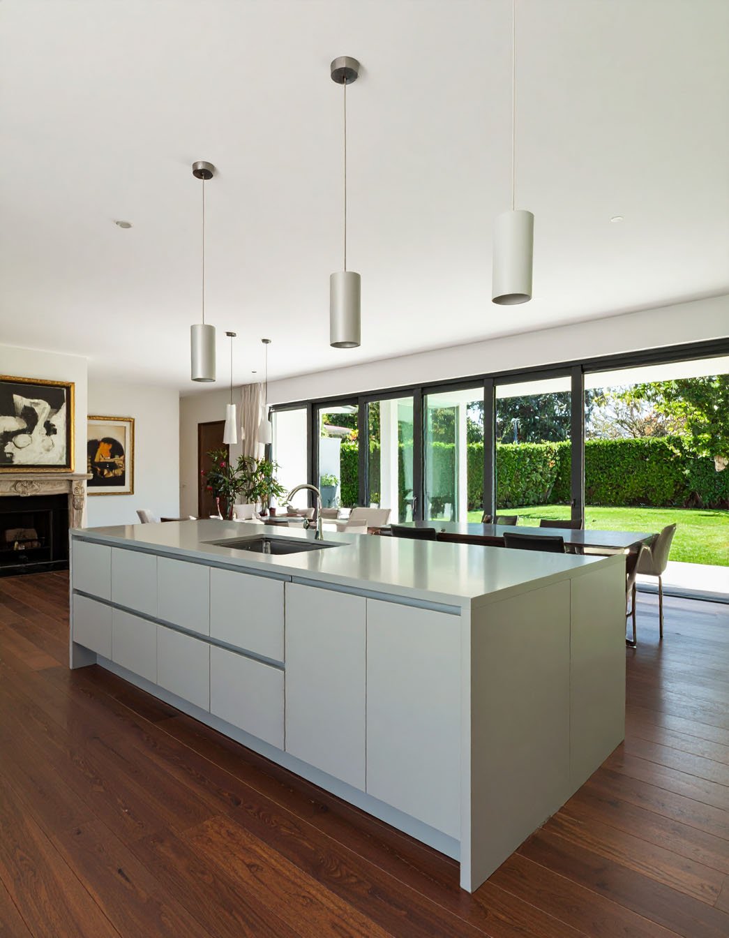 Cuisine ouverte moderne avec grand îlot gris clair, suspensions cylindriques et vue sur jardin