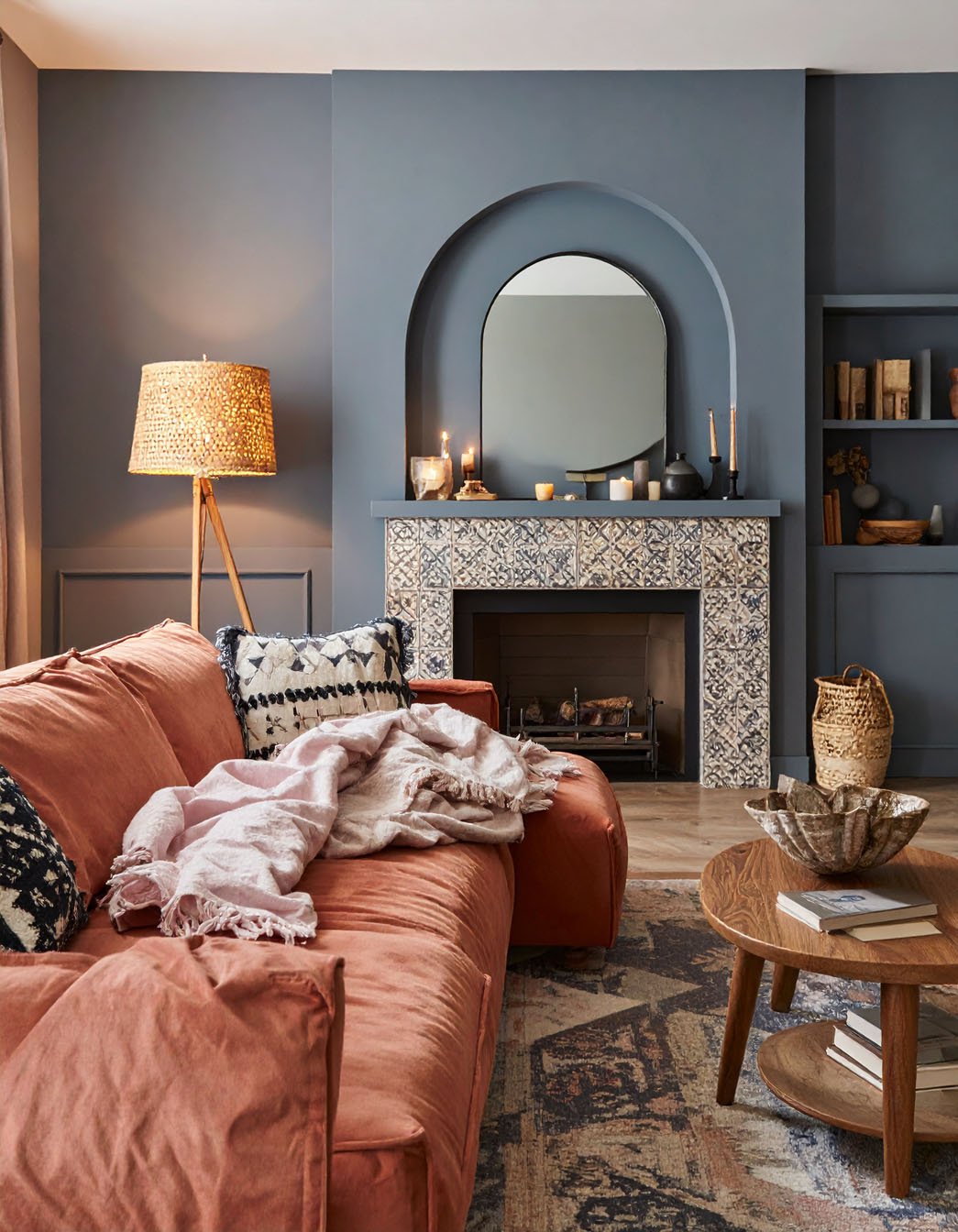 Salon avec murs bleu-gris, canapé couleur rouille et cheminée avec carreaux à motifs