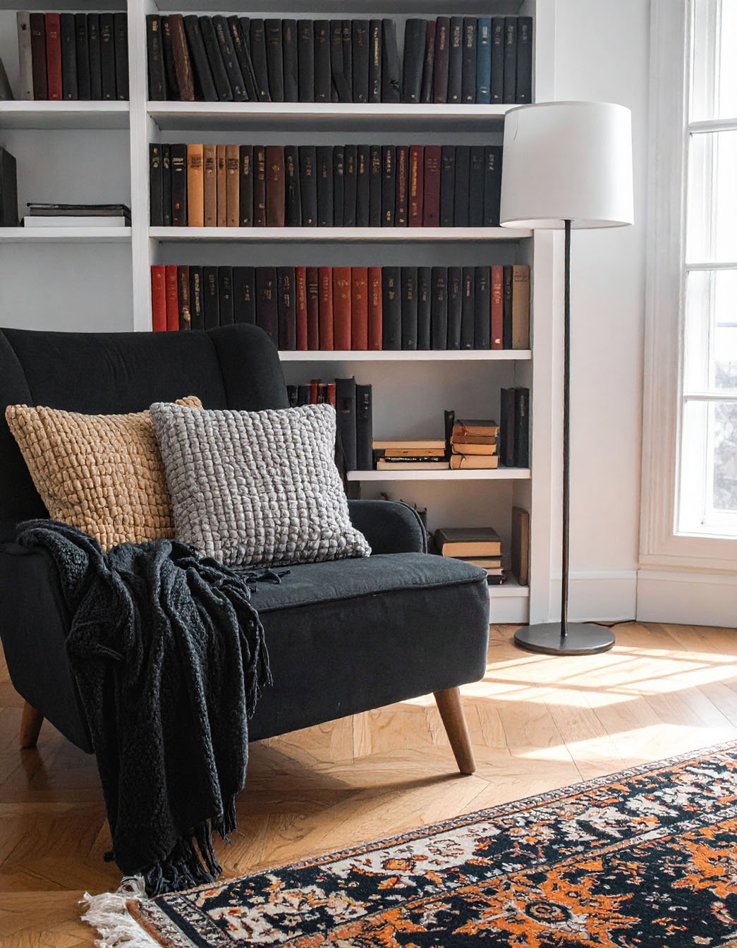 Coin lecture avec fauteuil noir, coussins texturés et bibliothèque remplie de livres