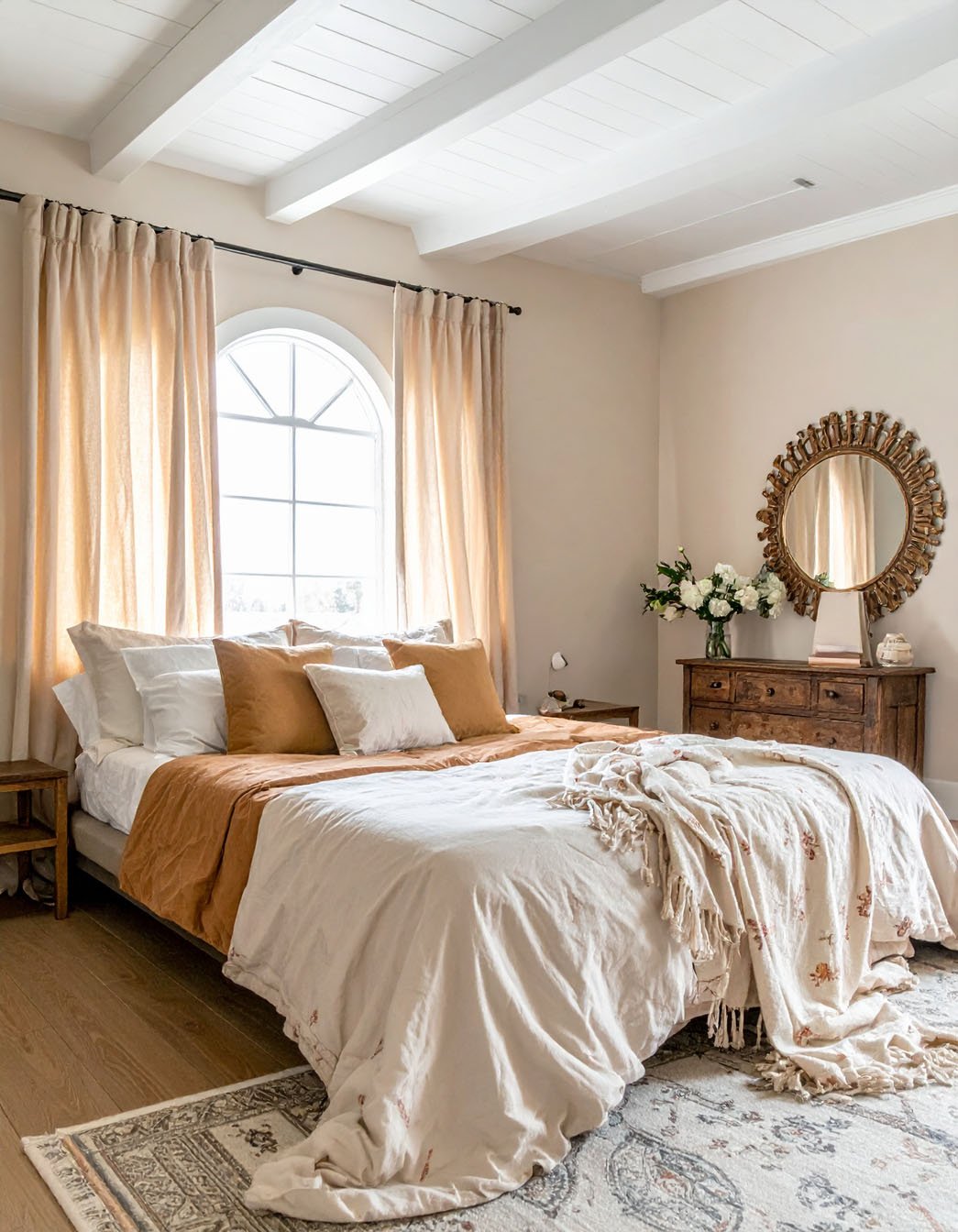 Chambre avec literie aux tons terreux, grande fenêtre cintrée et miroir soleil