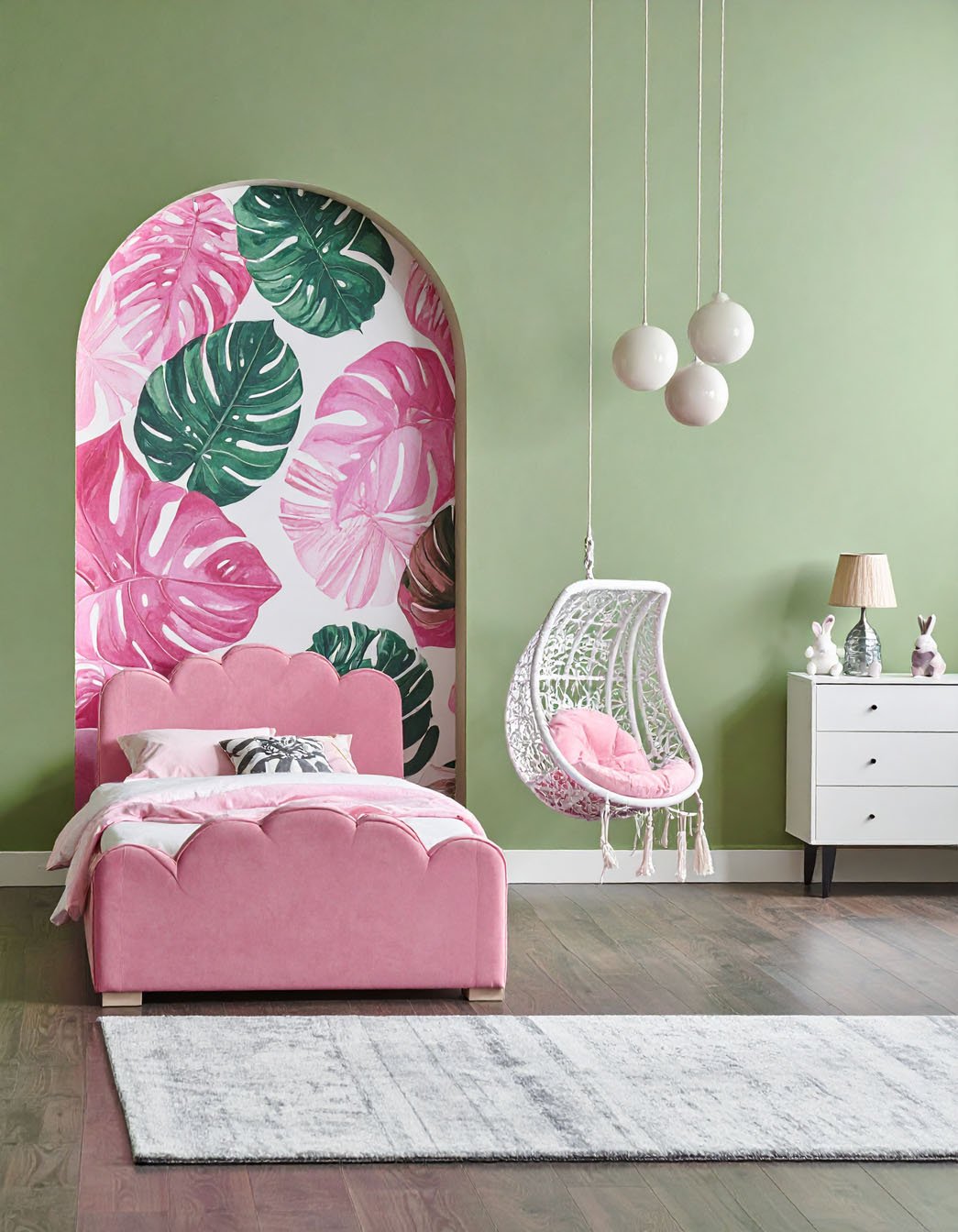 Chambre d'enfant avec murs verts, lit rose festonné, fauteuil suspendu et niche avec papier peint à motif de feuilles de monstera