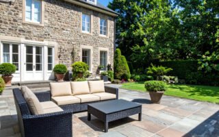 Terrasse en gravier avec table et chaises en fer forgé, entourée de buis et de fleurs