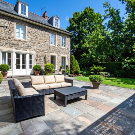 Terrasse en gravier avec table et chaises en fer forgé, entourée de buis et de fleurs