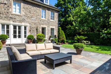 Terrasse en gravier avec table et chaises en fer forgé, entourée de buis et de fleurs