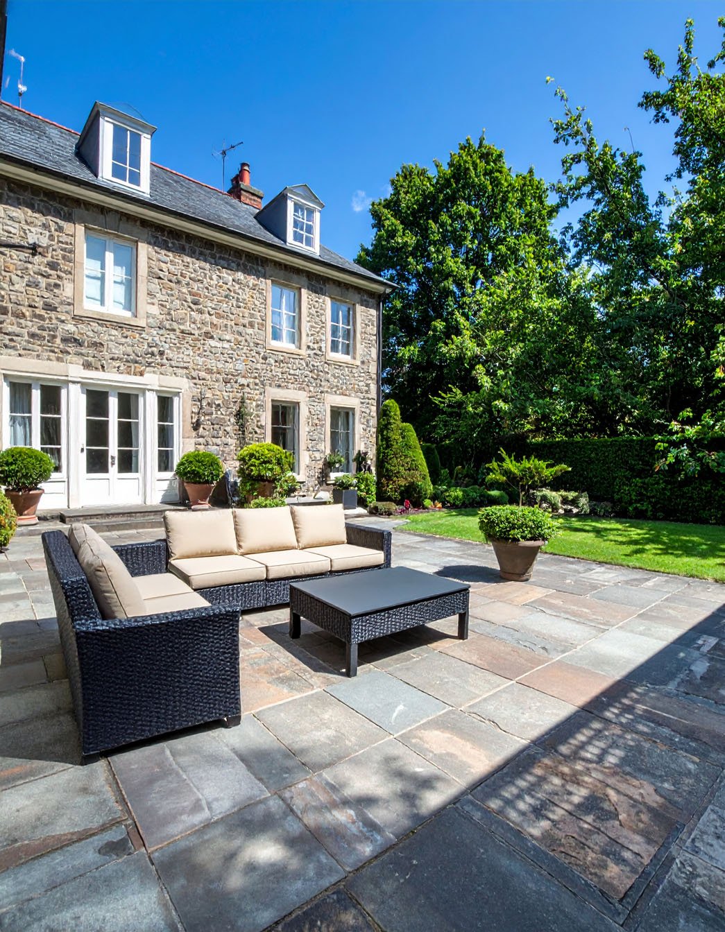 Terrasse en gravier avec table et chaises en fer forgé, entourée de buis et de fleurs