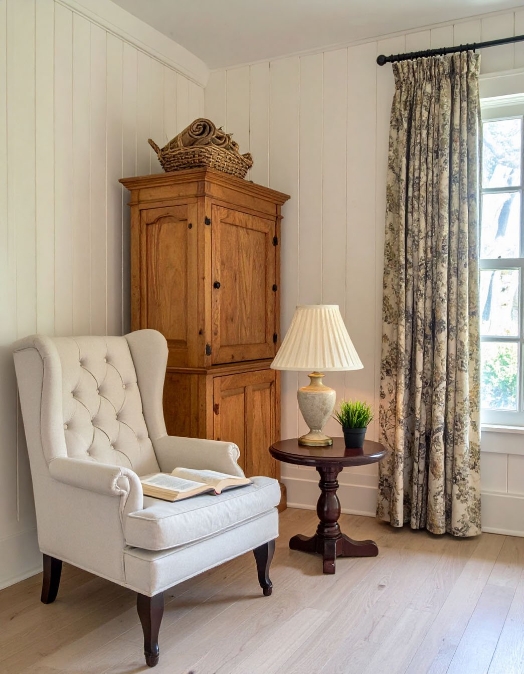 Coin lecture avec fauteuil bergère beige, armoire ancienne en bois et rideaux à motifs