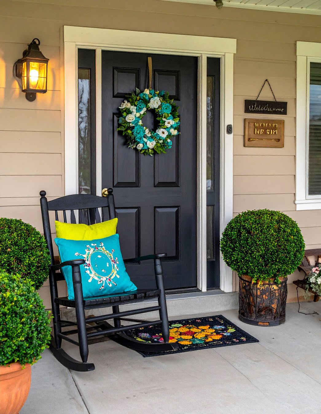 Porte d'entrée noire avec couronne florale bleue et blanche, fauteuil à bascule noir