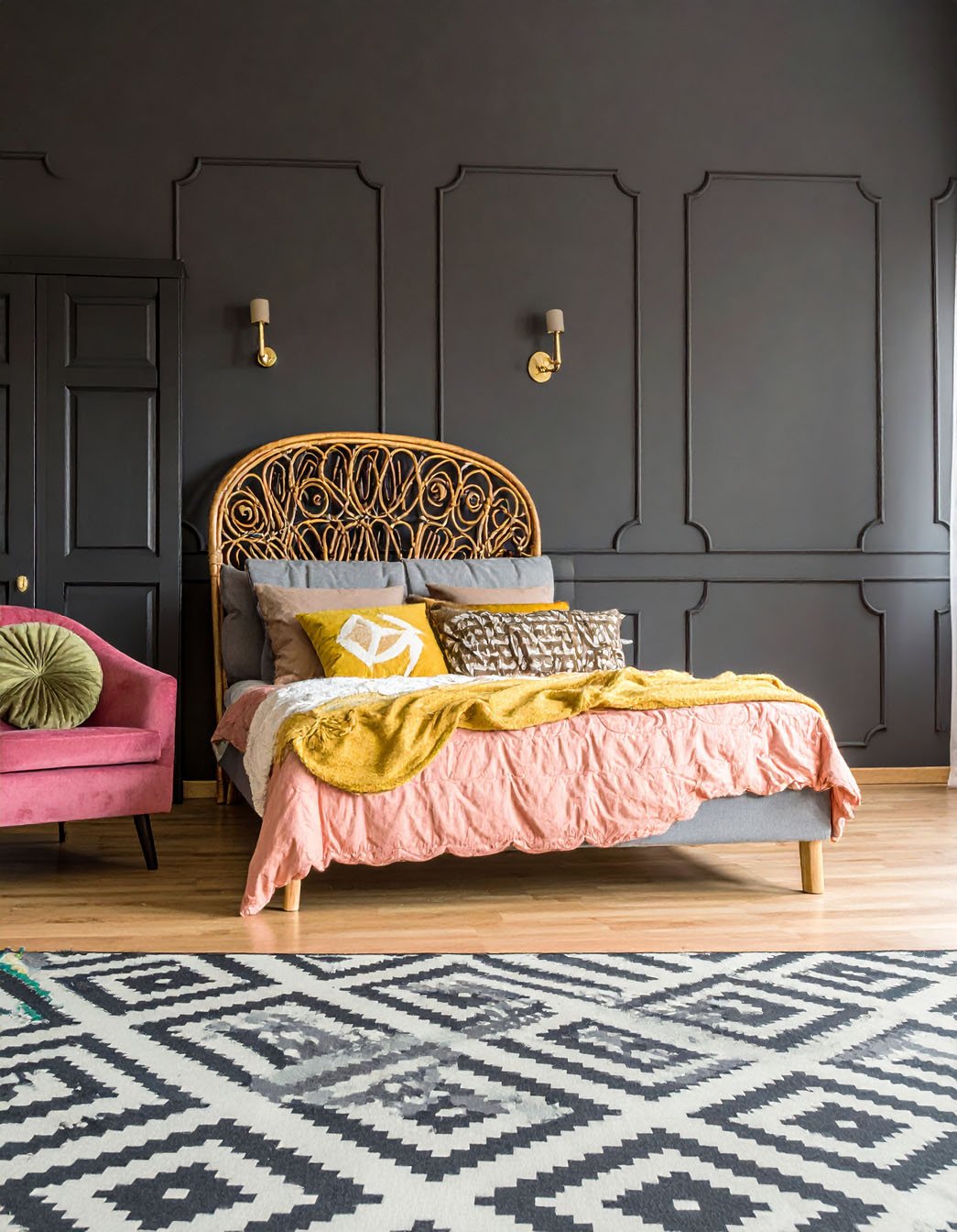 Chambre avec murs noirs à moulures, lit avec tête de lit en rotin et tapis à motifs géométriques