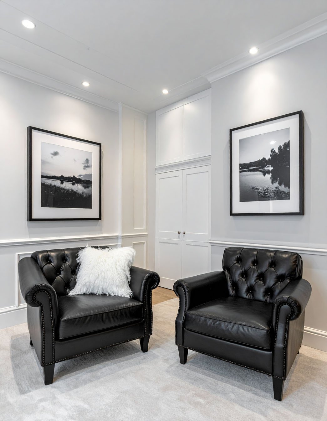 Salon avec deux fauteuils club en cuir noir et photographies de paysages en noir et blanc