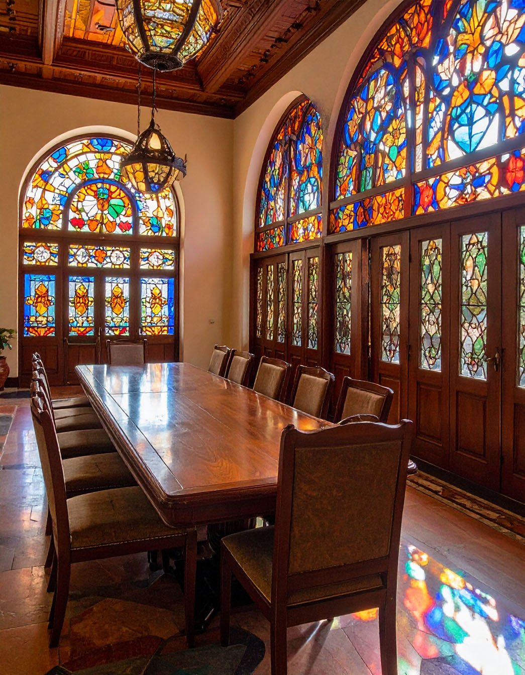 Salle à manger majestueuse avec longue table en bois et grandes fenêtres à vitraux colorés
