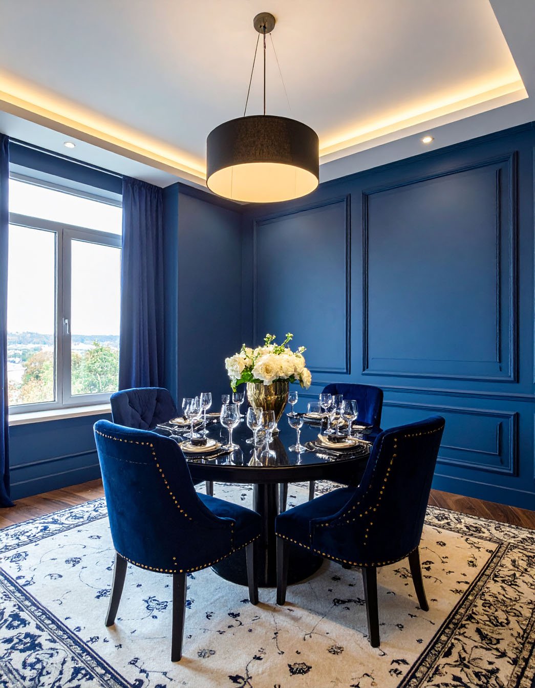 Salle à manger avec murs et chaises en velours bleu marine, table ronde noire et lustre