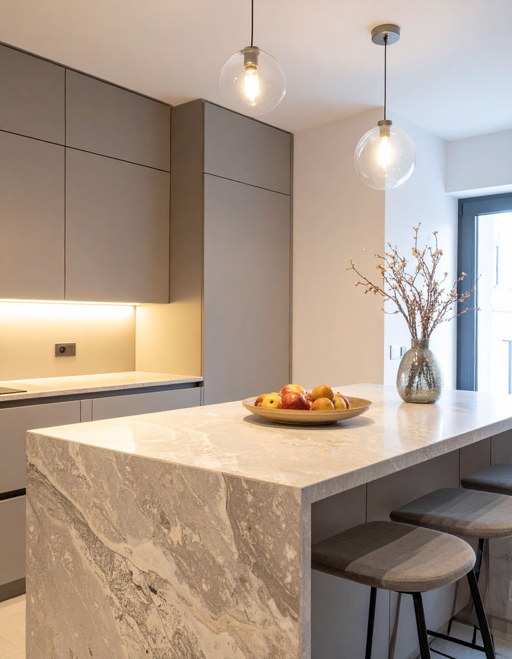 Cuisine moderne avec îlot en marbre gris, meubles taupe et suspensions globes en verre
