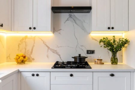Cuisine blanche avec crédence en marbre, éclairage sous les meubles hauts et suspension