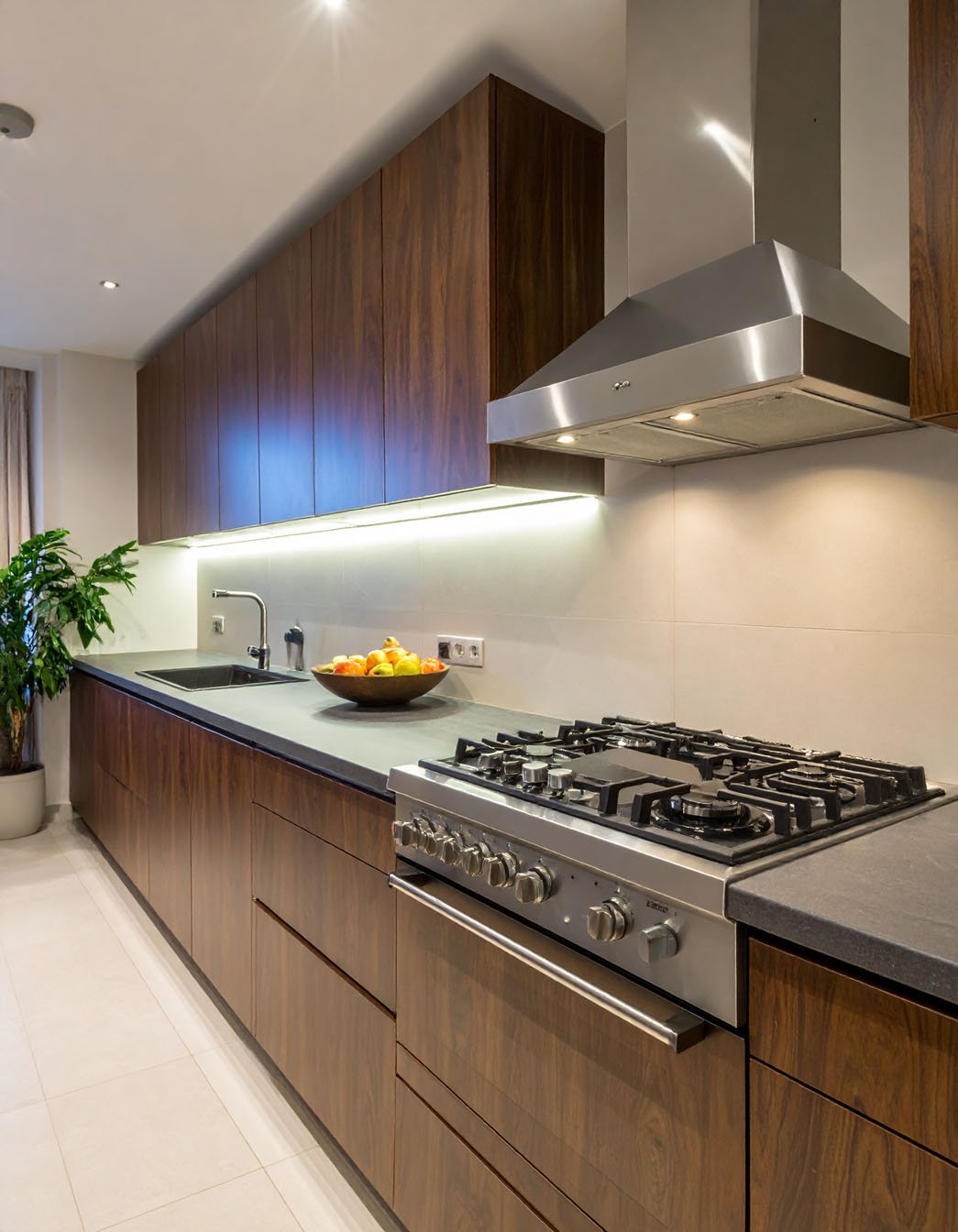 Cuisine avec meubles en bois foncé, plan de travail sombre et piano de cuisson inox