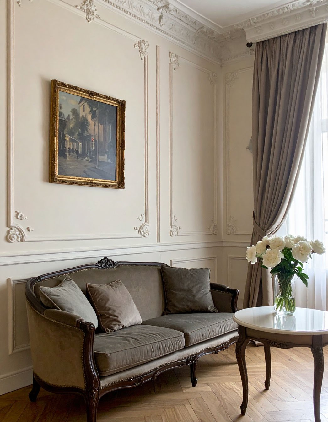 Salon de style parisien avec murs à moulures, canapé en velours taupe et bouquet de pivoines