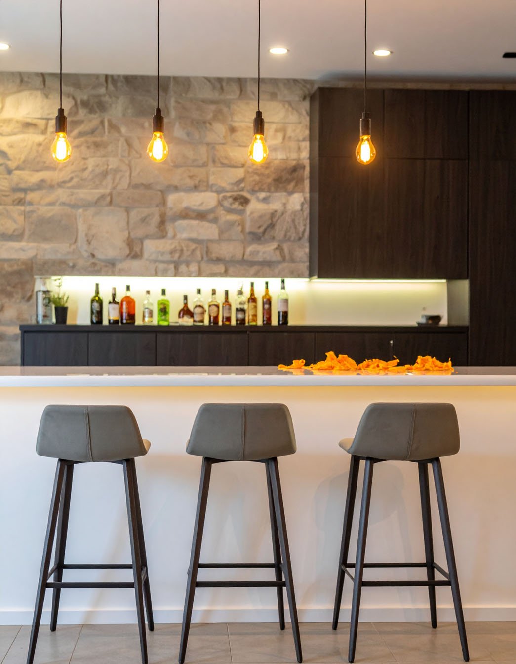 Bar avec comptoir blanc lumineux, tabourets hauts gris et mur en pierres apparentes